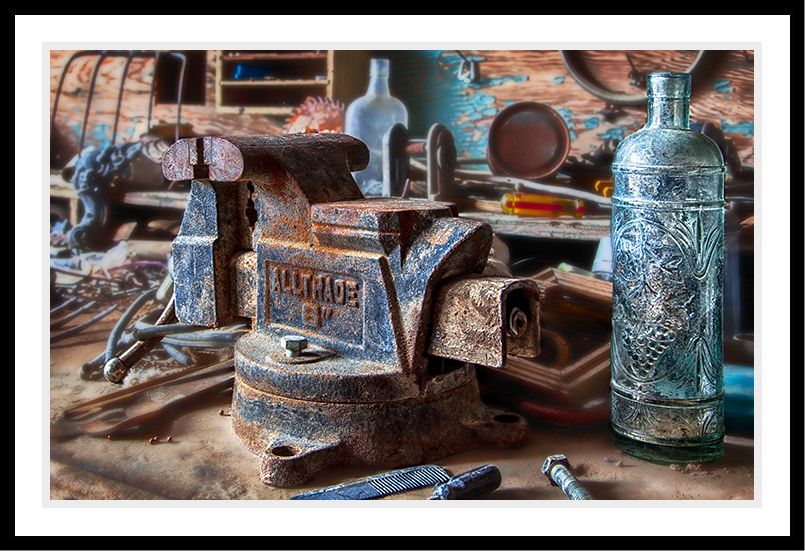 Still life of vise and bottle on workbench.